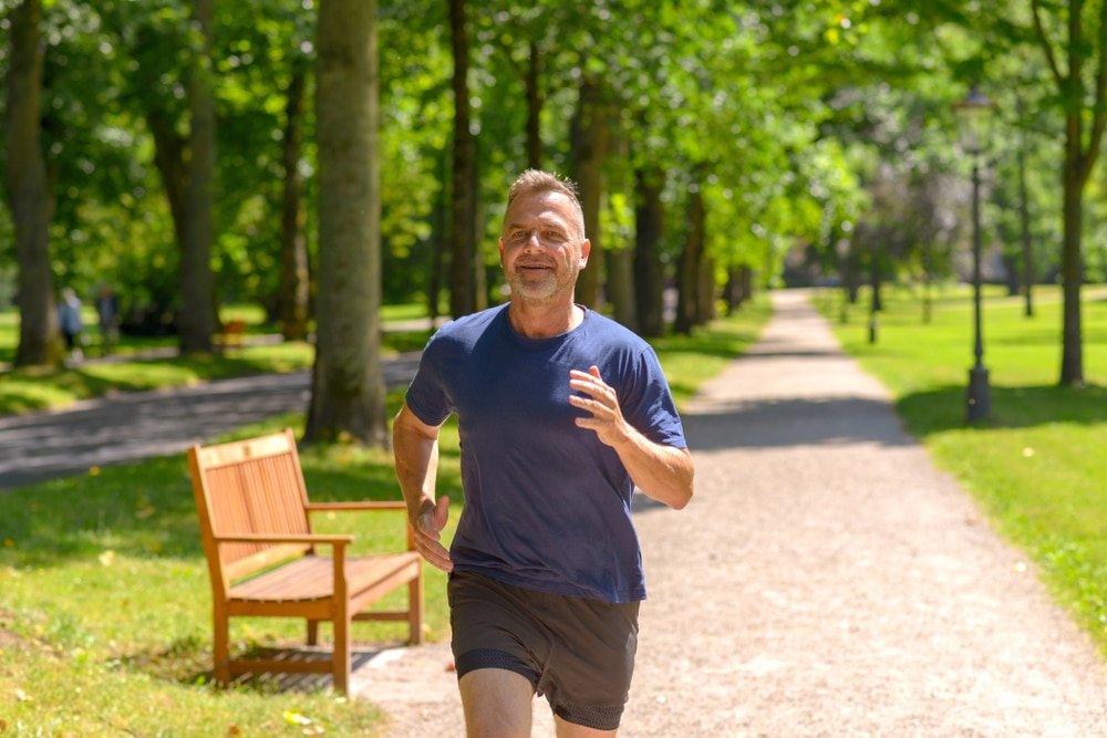 Middle,Aged,Man,Jogging,Along,Alley,In,Park,On,Sunny
